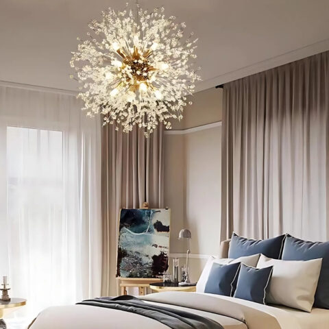 Lustre chambre doré de style nordique et moderne en forme de pissenlit allumé dans une chabre. Le lit double se trouve contre un mur beige et marron. La literie est blanche et bleue.Sur la gauche, on aperçoit une grande fenêtre avec à sa droite un tableau peint.