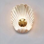 Sur un fond blanc on voit une applique murale en forme de coquillage blanche et dorée.
