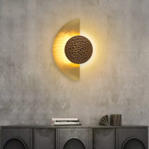 Sur un mur gris foncé on voit une applique murale au centre accrochée en forme de demi-lune dorée et allumée.