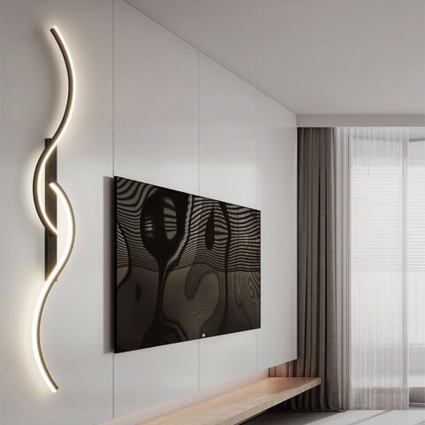 Photo d'un grand mur blanc sur lequel est accroché un grand écran TV, a sa gauche une applique murale allumée design en forme de 2 S, un en haut, l'autre en bas qui s'entremêle sur un socle rectangulaire noir. On voit une fenêtre dans le fond à droite.