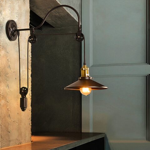 Applique murale en fer forgé style vintage avec poulie, armature noir, positionné dans une pièce sombre à côté d'une porte