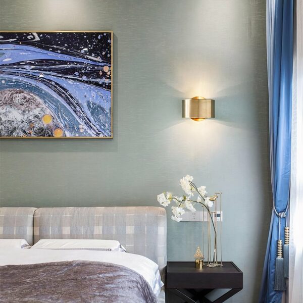 Applique murale en laiton minimaliste et moderne, de couleur dorée dans une chambre à côté d'un lit