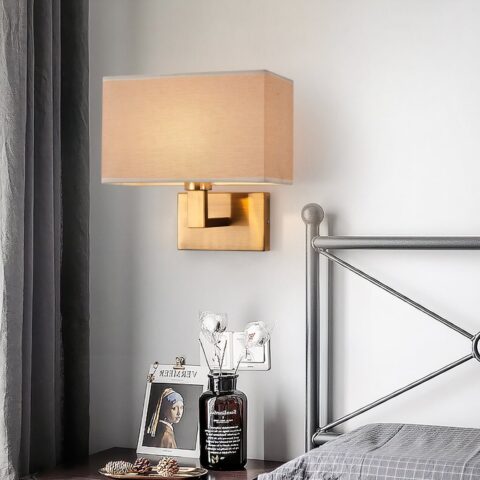 Applique murale en tissu marron, avec support en métal de couleur doré, à côté d'un lit.