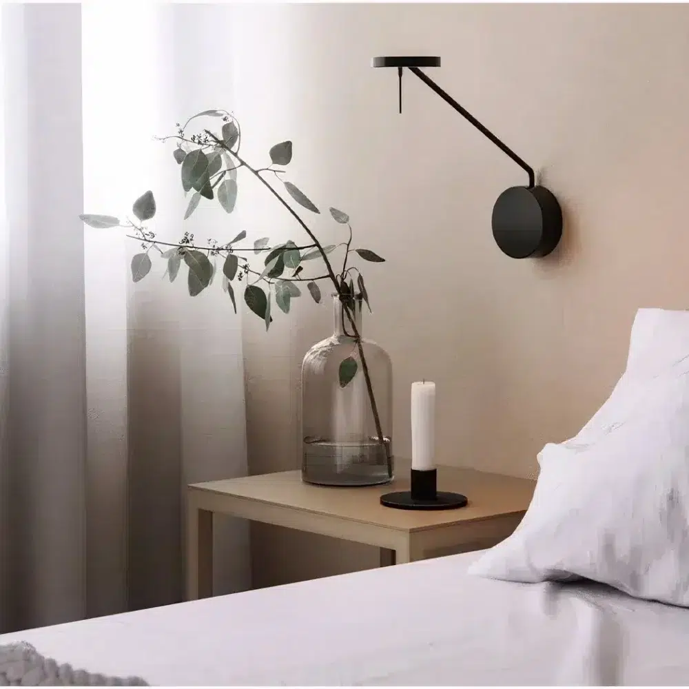 Applique murale noire design accrochée à un mur dans une chambre, au-dessus d'un lit t d'une table de chevet avec de la décoration