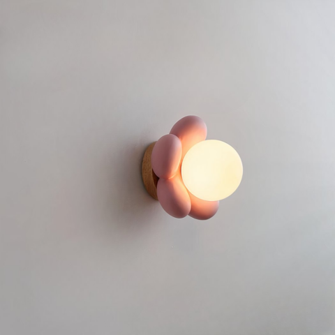 Sur un fond blanc on voit une applique murale en forme de fleur rose allumée.