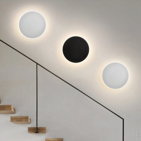 Sur un fond blanc on voit trois appliques murales rondes, deux blanches et une noire.