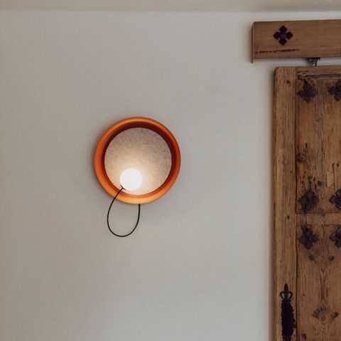 Applique murale terracotta et ronde, avec une ampoule dans le rond, positionné sur un mur à côté d'une porte en bois