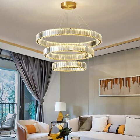 Grand lustre LED circulaire en cristal chromé or allumé et installé dans un salon, au-dessus d'un canapé blanc.
