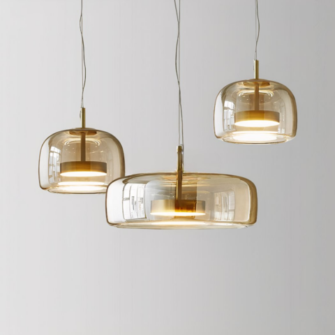Trois luminaires en verre suspendus, un grand au centre et deux plus petits sur les côtés, celui de droite est plus haut que celui de gauche. Sur un fond gris.