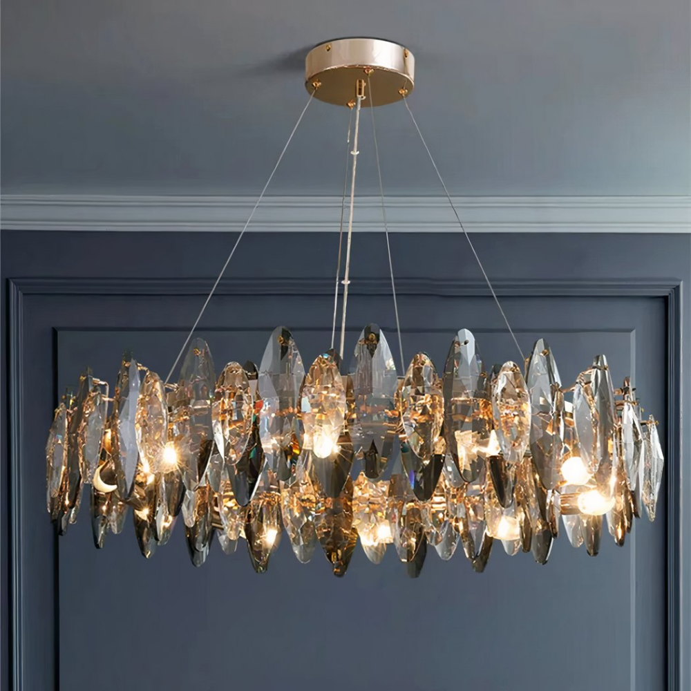 Grand lustre suspendu allumé en forme de couronne, avec des cristaux. Un mur gris anthracite dans le fond et un plafond gris clair.
