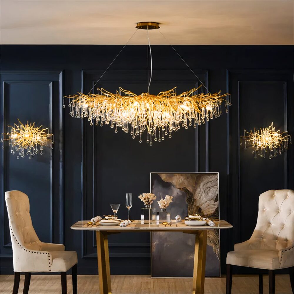 Lustre cuisine long et doré à design de gouttes d'eau sur fond bleu foncé avec une table et des fauteuils