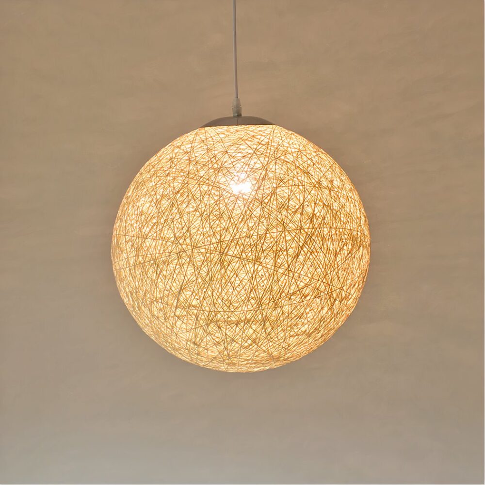 Lustre boule en corde avec ampoule allumée. Un mur beige en fond.