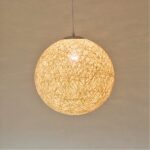 Lustre boule en corde avec ampoule allumée. Un mur beige en fond.