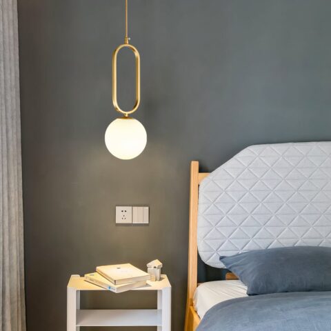 Suspension dorée en pierre de verre au design moderne sur fond gris avec un lit à droite