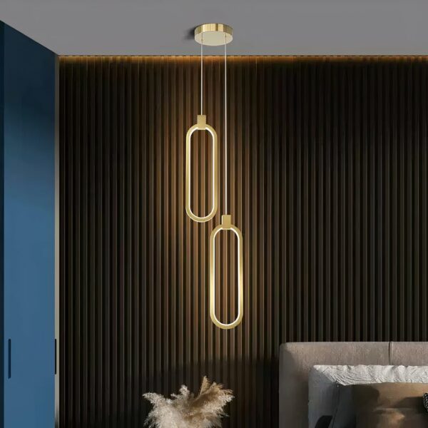 Suspension dorée LED au design minimaliste en aluminium sur fond noir avec un lit à droite