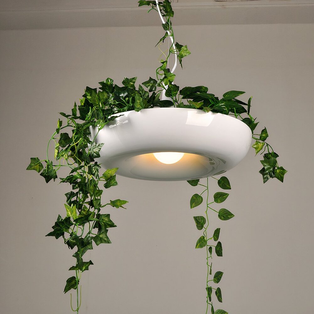 Lumière suspendu, avec abat-jour donuts blanc, dans lequel il y a une plante verte tombante. Au fond un mur blanc.