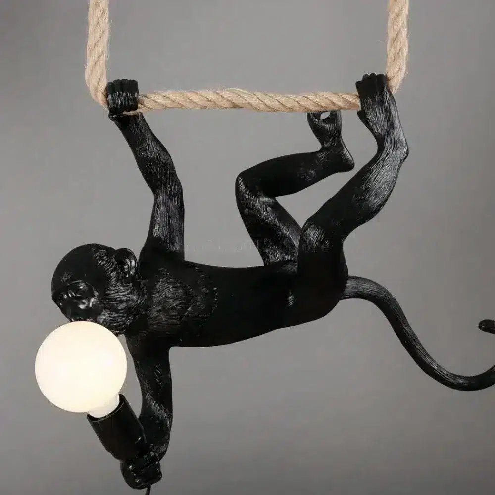 Suspension singe noire accrochée à l'envers à une corde tenant une ampoule ronde