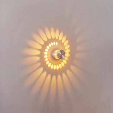 Applique murale LED circulaire en aluminium argenté allumée, projetant une spirale de lumière chaude sur un mur blanc