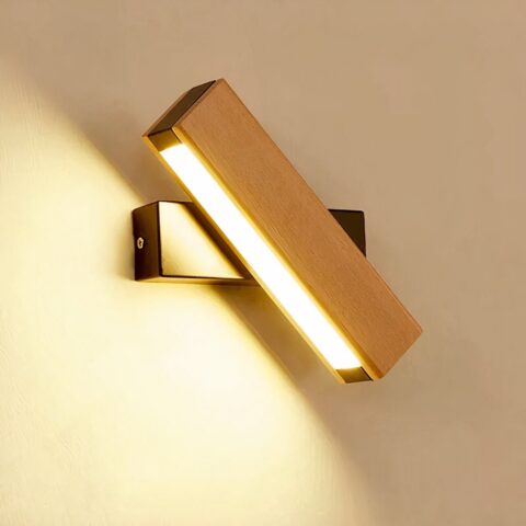 Applique murale LED, rectangulaire en bois, sur un socle rectangulaire noir. Le rectangle en bois avec la source lumineuse est de trois-quart, tandis que le socle noir est horizontal. La lumière est allumée. L'applique est accrochée sur un mur beige.