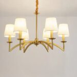 Lustre doré en métal en forme de chandelier avec 6 abat-jours en tissus blanc. sur un fond gris.