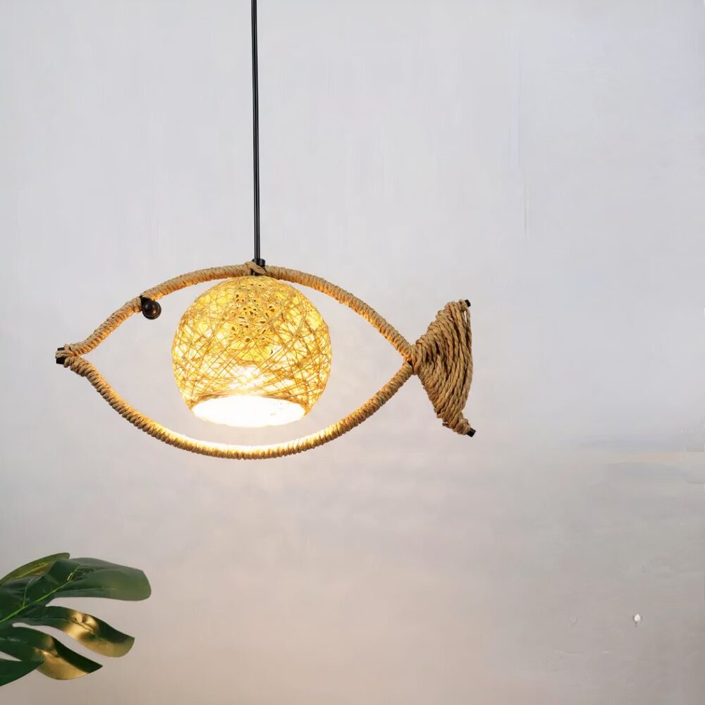 Lustre en corde enroulée autour d'une tige métallique en forme de poisson, suspendu. Avec une abat-jour au centre en forme de boule. Derrière on voit un mur gris et en bas à gauche on voit un morceau de plante verte.