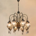 Lustre marocain en métal et en boules de verre craquelé. Composé de 8 boules accrochées au lustre par des bras recourbés. Et chacune habillé de genre de broderies métalliques. Sur un fond beige.