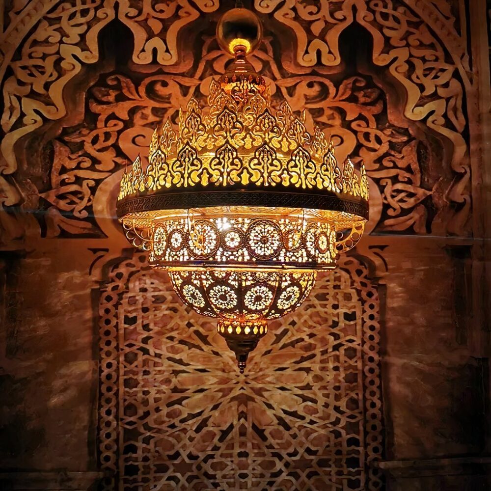 Lustre en laiton ajouré suspendu devant un panneau mural sculpté à motifs géométriques