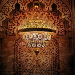 Lustre en laiton ajouré suspendu devant un panneau mural sculpté à motifs géométriques