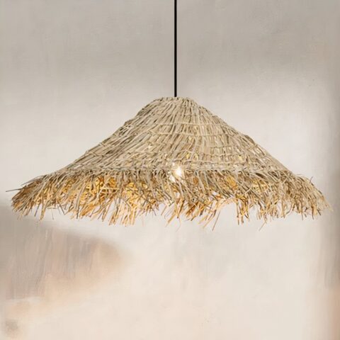 Lustre en paille suspendu, de forme conique comme un chapeau. En paille tressé, avec les bords en paille brossé. Derrière on voit un mur beige et à droite un bout de l'ombre de l'abat-jour.