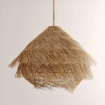 Lustre en paille suspendu, en forme de hutte, recouvert de paille effet brossée. Sur un fond beige.