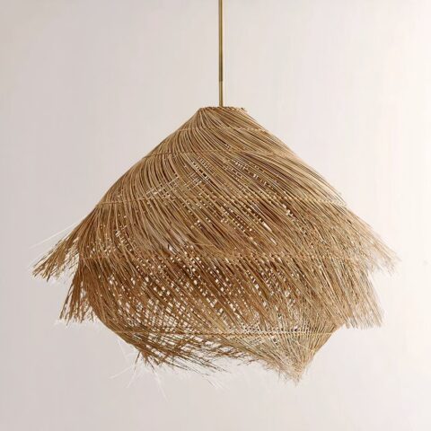 Lustre en paille suspendu, en forme de hutte, recouvert de paille effet brossée. Sur un fond beige.