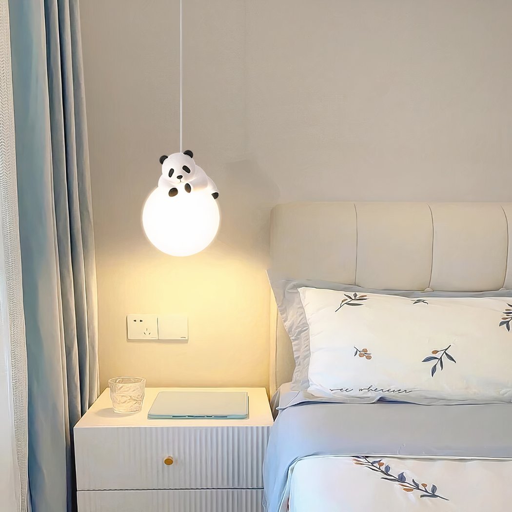 Lustre boule suspendue, avec un panda couché dessus. Au-dessus d'une table de chevet blanche avec un tiroir, à côté d'un lit. Le mur derrière est blanc.