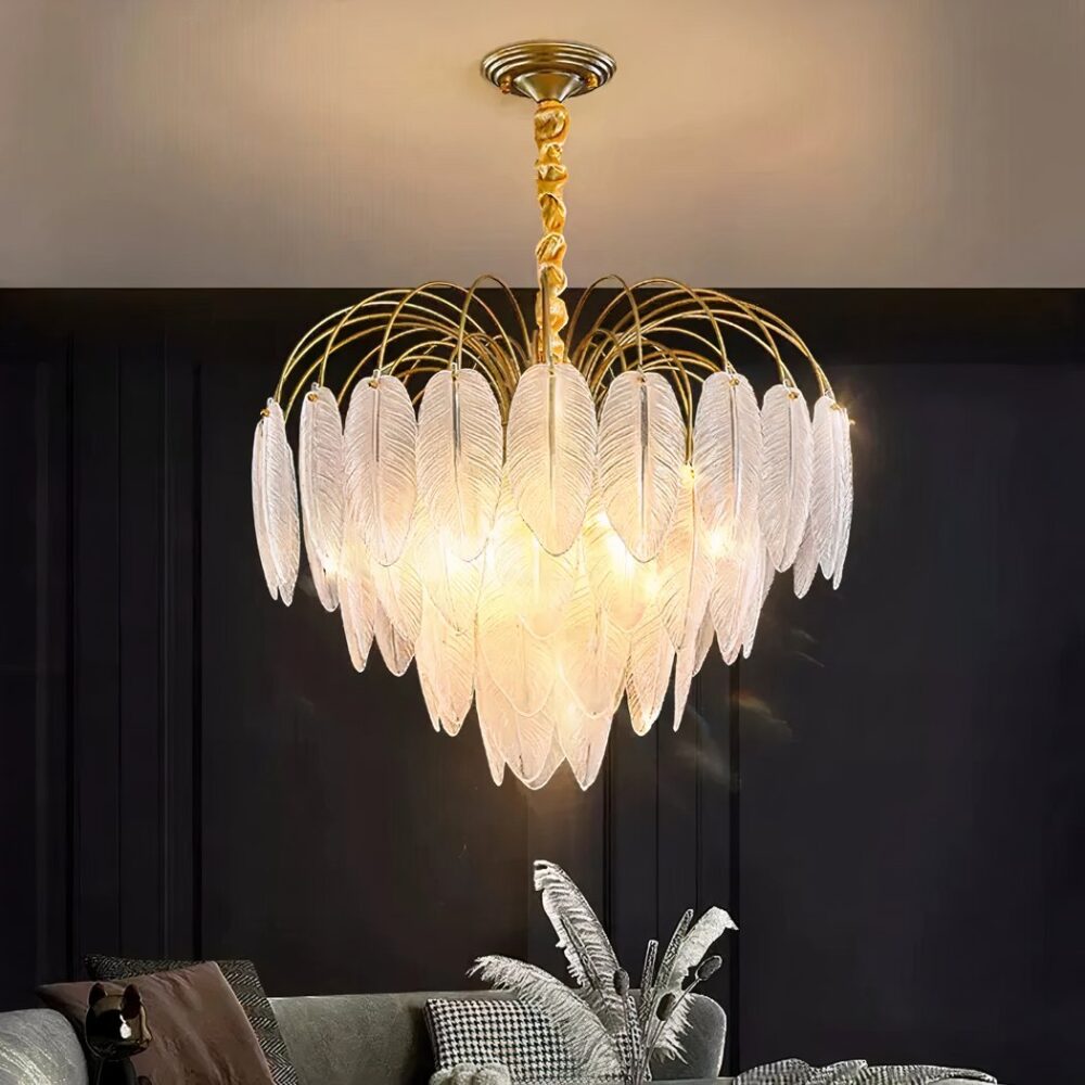 Lustre plumes en verres en forme de grappe. Allumé et installé dans un salon avec le mur du fond noir et un canapé gris. Le plafond est blanc et on voit le reflet de la lumière dessus.