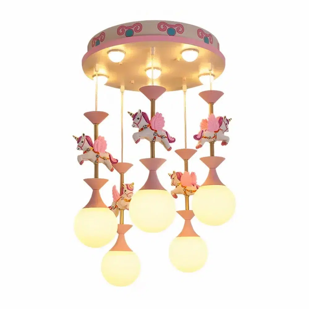 Lustre Rose Carrousel Licorne Led Pour Chambre D Enfant Lustre carrousel, avec des licornes, rose et blanc. Avec 5 ampoules allumées suspendues sous les licornes. Sur un fond blanc.