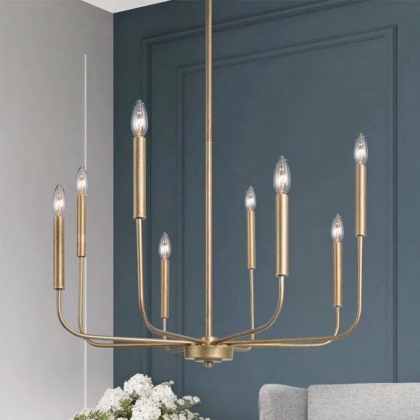 Lustre en métal doré, en forme de chandelier avec 8 bougies à ampoule. Derrière, au fond, on voit un mur bleu canard, un bout de bouquet de fleurs blanches et un bout de canapé gris clair.