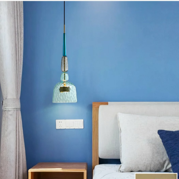 Lustre suspendu LED moderne en verre coloré sur fond bleu avec un lit à droite