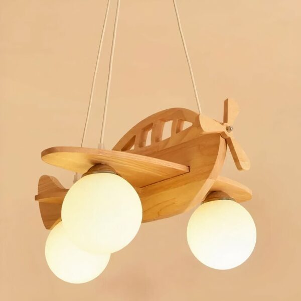 Suspension en forme d'avion, en bois, avec 3 boules blanche pour les ampoules. Suspendu par 3 fils à un socle en bois accroché au plafond. Sur fond beige.