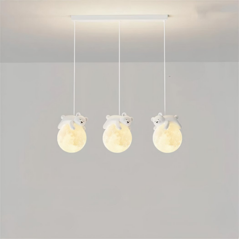 Luminaire suspendus, composé de trois câbles avec chacun une boule qui représente la lune, et un nounours qui dort sur la lune. Les boules sont allumées. Le socle rectangulaire est accroché au plafond gris clair, on voit dans le fond un mur gris clair aussi.