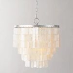 Suspension en nacre suspendue par une chaine argentée. Composé d'une armature ronde argenté orné de perles de nacre plates et rectangulaires qui forme une grappe. Sur un fond gris.