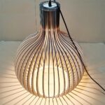 Lustre DIY en bois massif de bambou, assemblé et allumé, sur fond beige.