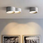 Lustre moderne LED au design minimaliste de cylindre et spot encastré en version blanche, fixé au plafond et allumé, dans un salon.