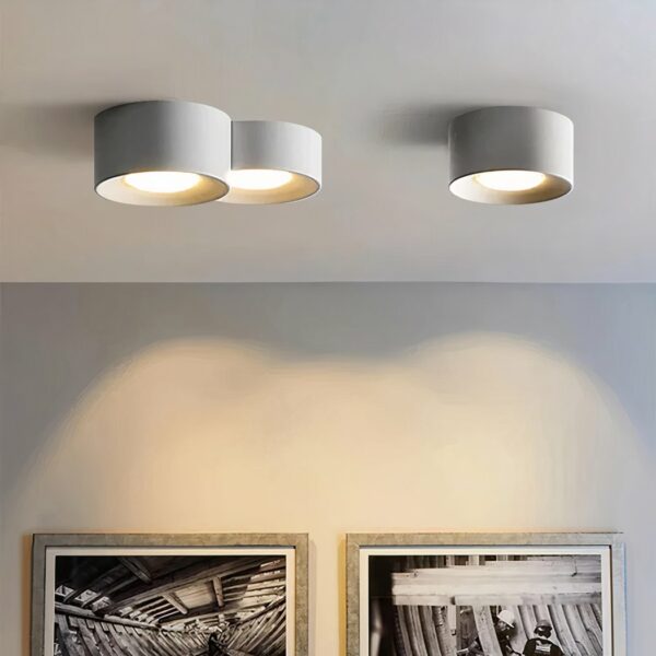 Lustre moderne LED au design minimaliste de cylindre et spot encastré en version blanche, fixé au plafond et allumé, dans un salon.