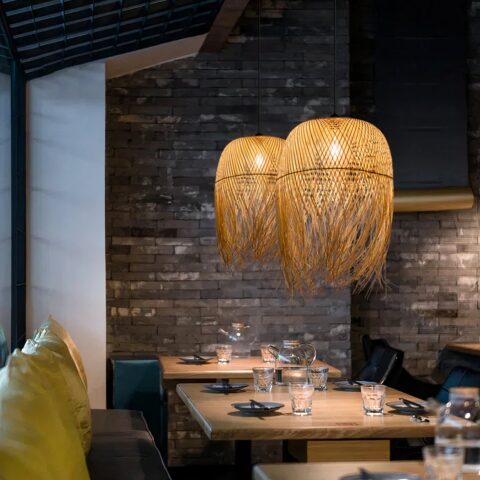 Lustre paille traditionnel tissé main suspendu et allumé au dessus de tables de salle à manger dans un environnement qui semble être un restaurant.