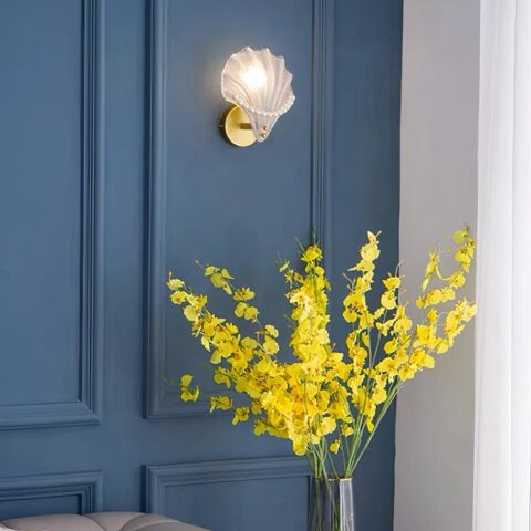 Applique murale en verre dépoli et perles accrochée au mur bleu d'un salon avec un bouquet de fleurs jaunes en dessous.