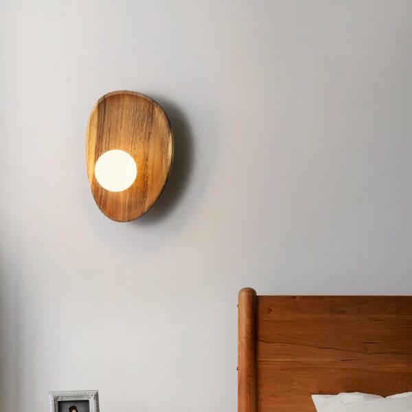 Applique murale en bois style coquillage avec sa perle lumineuse petit modèle accrochée au mur d'une chambre, à côté du lit.