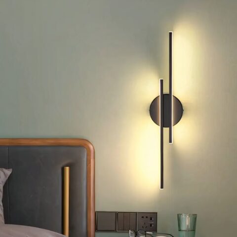 Applique murale linéaire design moderne accrochée sur le mur d'une chambre à coucher et allumée, à côté du lit.