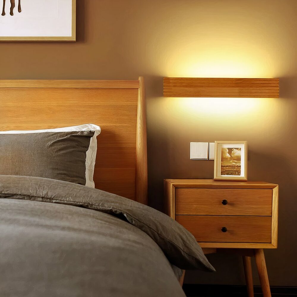 Applique murale escalier design en bois accrochée dans une chambre à coucher et allumée, à côté du lit, sur un mur taupe.