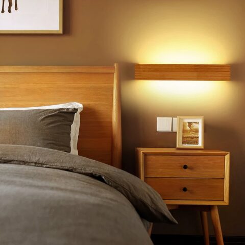 Applique murale escalier design en bois accrochée dans une chambre à coucher et allumée, à côté du lit, sur un mur taupe.