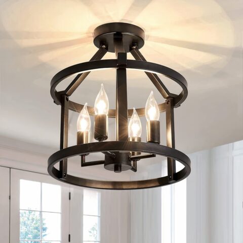 Lustre plafonnier noir en forme de chandelier avec 4 ampoules allumées au centre. Elles sont dans une structure avec 2 cercles noirs en métal. Le cercle du haut est tenu par des barres en métal noir au support rond fixé au plafond. En bas derrière, on aperçoit des fenêtres aux encadrements blancs.