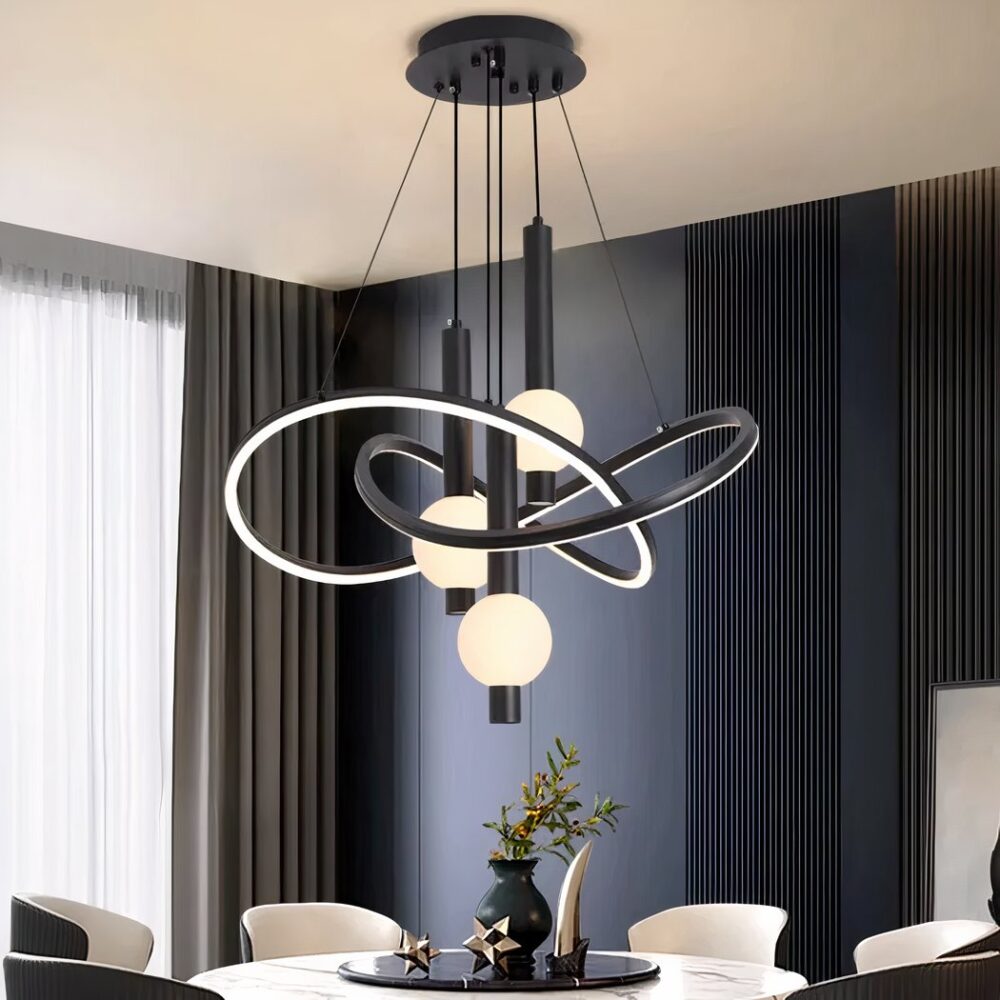 Lustre noir avec support noir fixé au plafond d'où descendent des câbles tenant des structures arrondies entrelacées lumineuses et noires à l'extérieur. Au centre de ces structures, sont pendus des tubes noirs avec une boule lumineuse allumée. Fixé au-dessus d'une table blanche ronde style marbre, avec plateau noir rond, un vase dessus et des objets de décoration. 6 fauteuils autour de la table,à gauche une baie vitrée avec un rideau gris et le mur en face est bleu canard avec des rainures verticales.